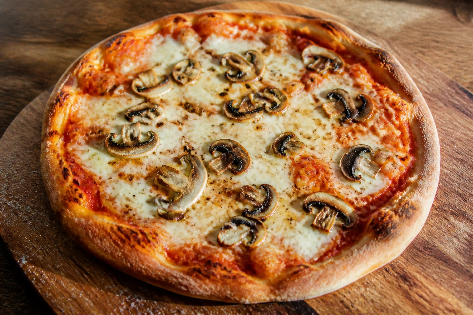 Pizza maison garnie de champignons de Paris dorés, sortie du four sur une planche en bois